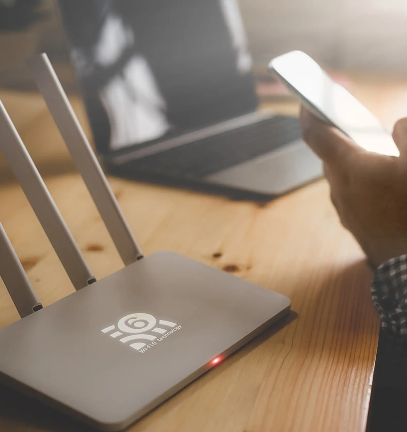 Ein moderner WLAN-Router auf einem Holzschreibtisch, daneben eine Person mit Smartphone