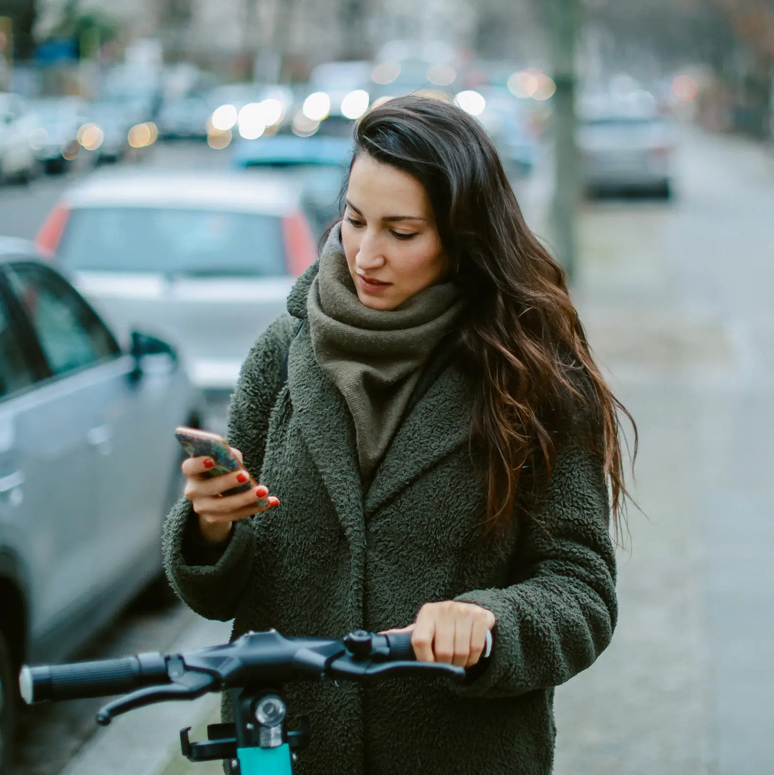 Junge Frau schaut beim Rollerfahren in der Stadt auf ihr Smartphone