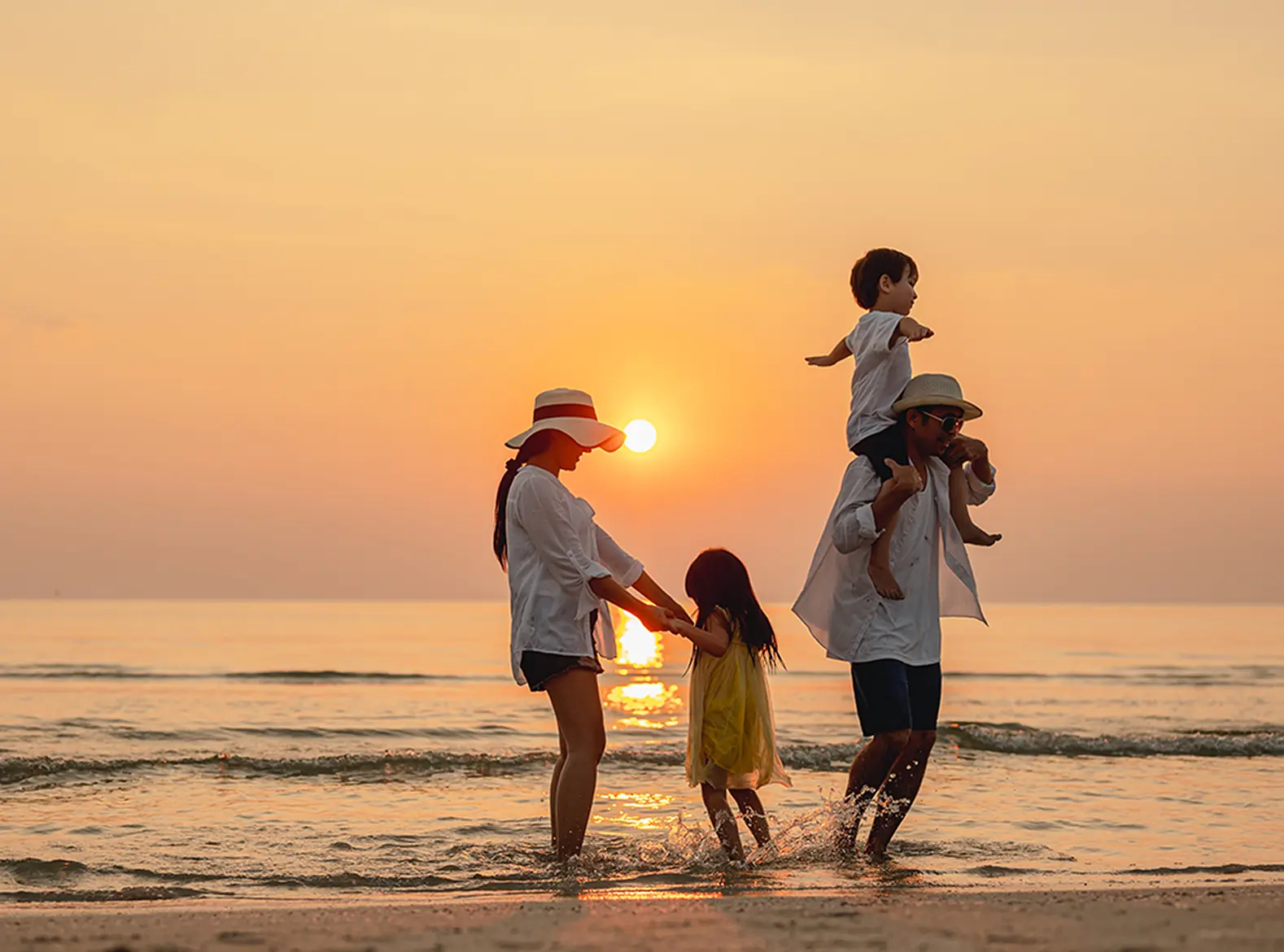 Familie am Strand bei Sonnenuntergang, Eltern mit Kindern im Wasser spielend