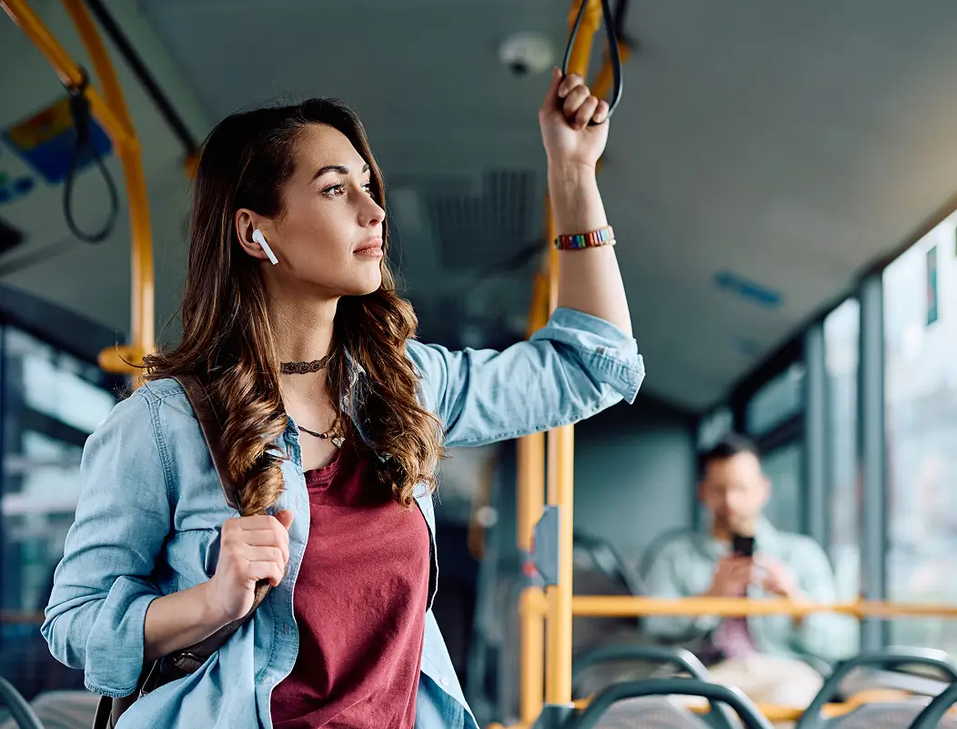 Junge Frau mit Kopfhörern fährt entspannt im Bus und schaut aus dem Fenster