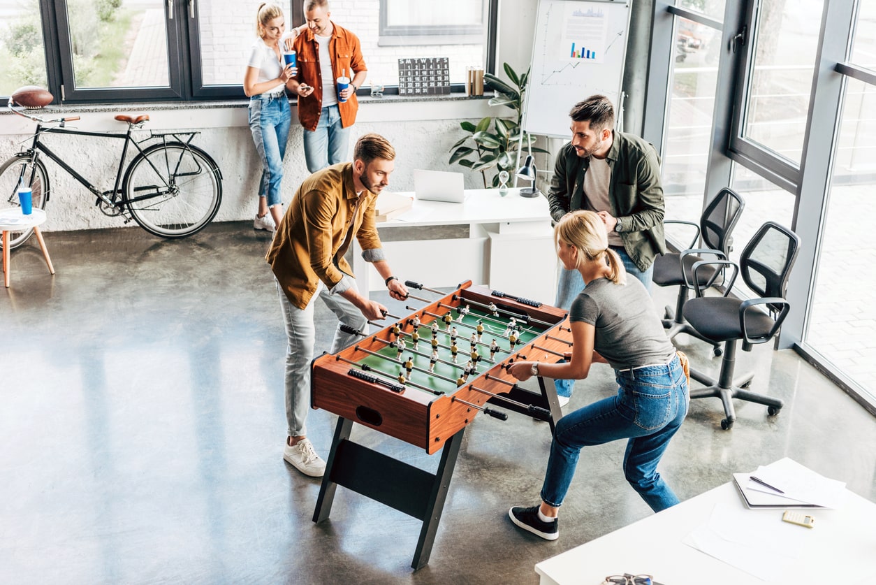 Illustration einer modernen und entspannten Unternehmenskultur: Mitarbeiter spielen Tischfußball im Büro, gefördert durch die Benefits von become.1