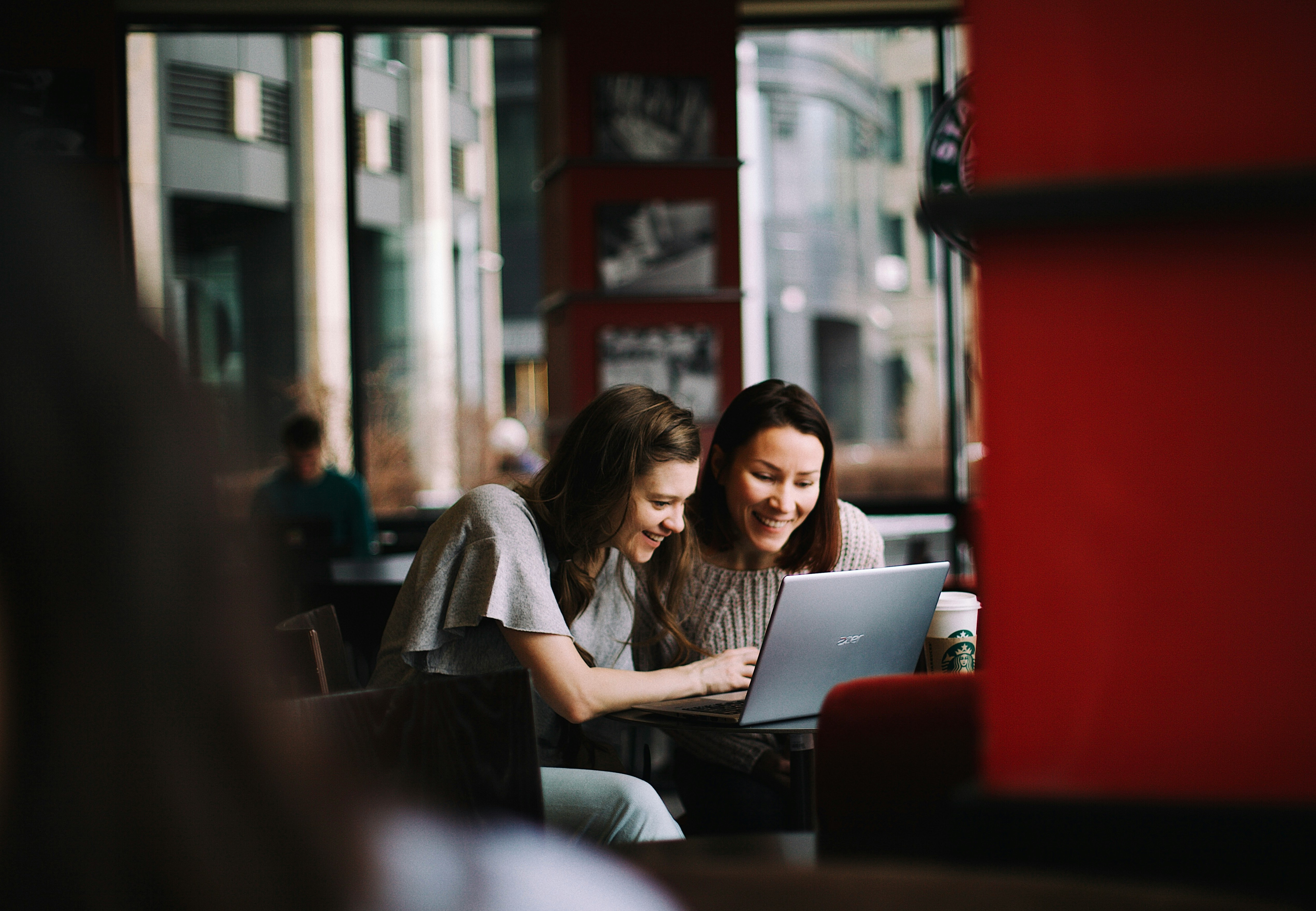 Zwei Frauen die gemeinsam lächlen auf einen Laptop schauen und reden