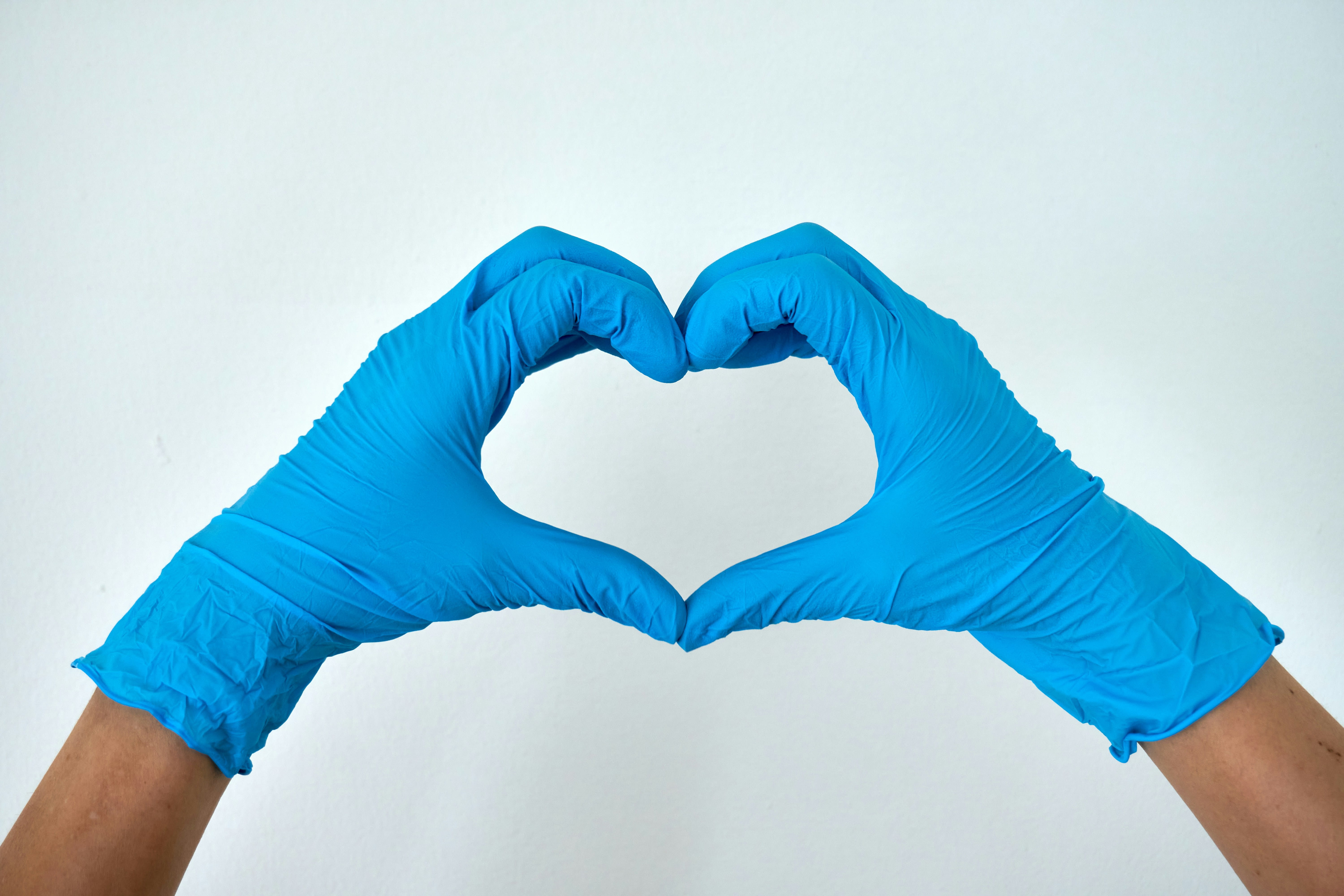 2 Hände mit blauen Gummihandschuhen formen ein Herz